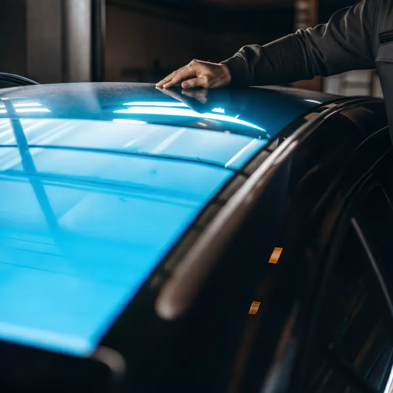 Eine Hand streicht über ein Fahrzeugdach um die Reparatur eines Fahrzeuges zu überprüfen